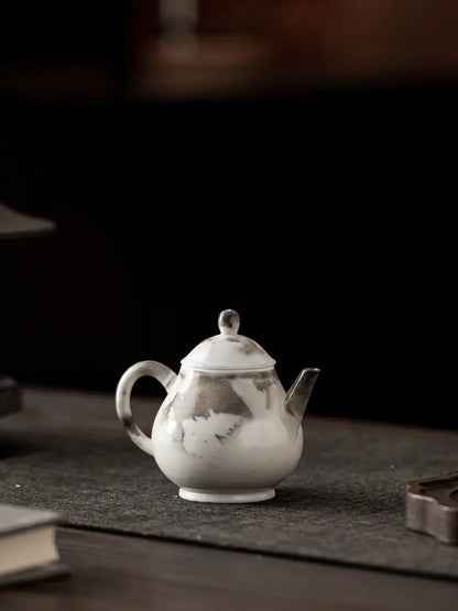 Small ink-wash ceramic teapot displayed on a dark tea table