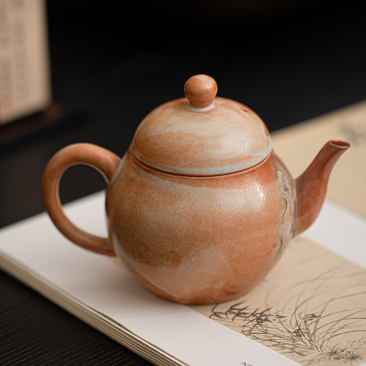 Liting handmade ceramic teapot displayed on an open art book