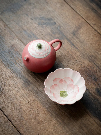 Top view of a pink lotus ceramic teapot with one flower-shaped teacup on a wooden table
