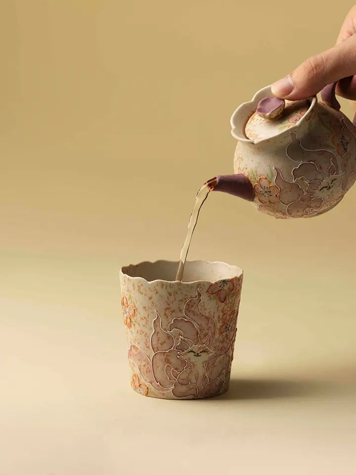 Tea being poured from a ceramic teapot into the hand-painted petal-rim coffee cup
