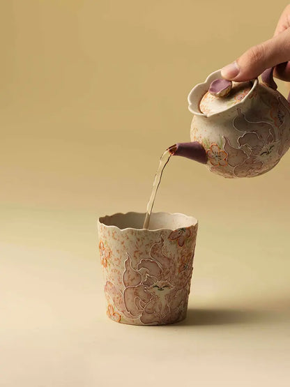 Tea being poured from a ceramic teapot into the hand-painted petal-rim coffee cup
