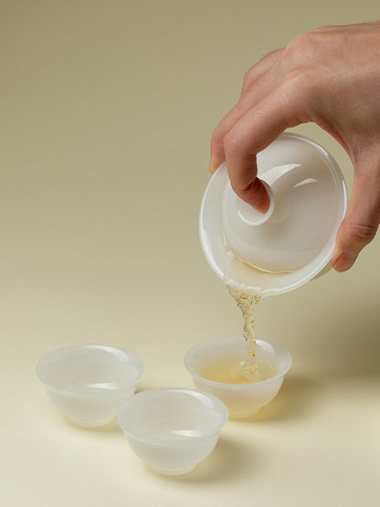 Tea being poured from a translucent ceramic gaiwan into one of three teacups

