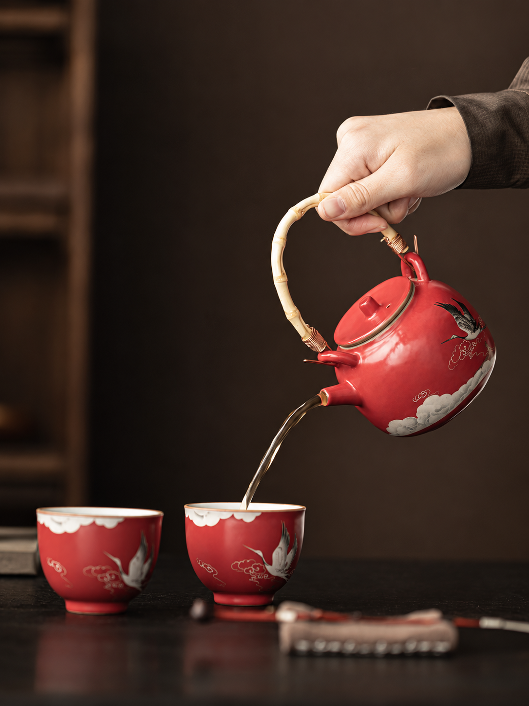 Chinese red crane teapot pouring tea into a matching ceramic cup
