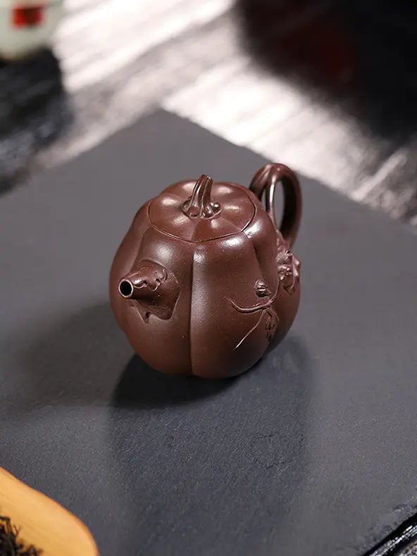 Overhead angled view of a deep reddish-brown pumpkin zisha teapot on a dark tea mat