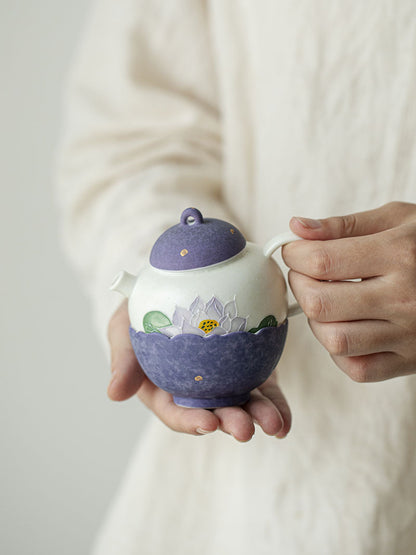 Hand-held purple lotus ceramic teapot showing its rounded body and hand-painted floral details