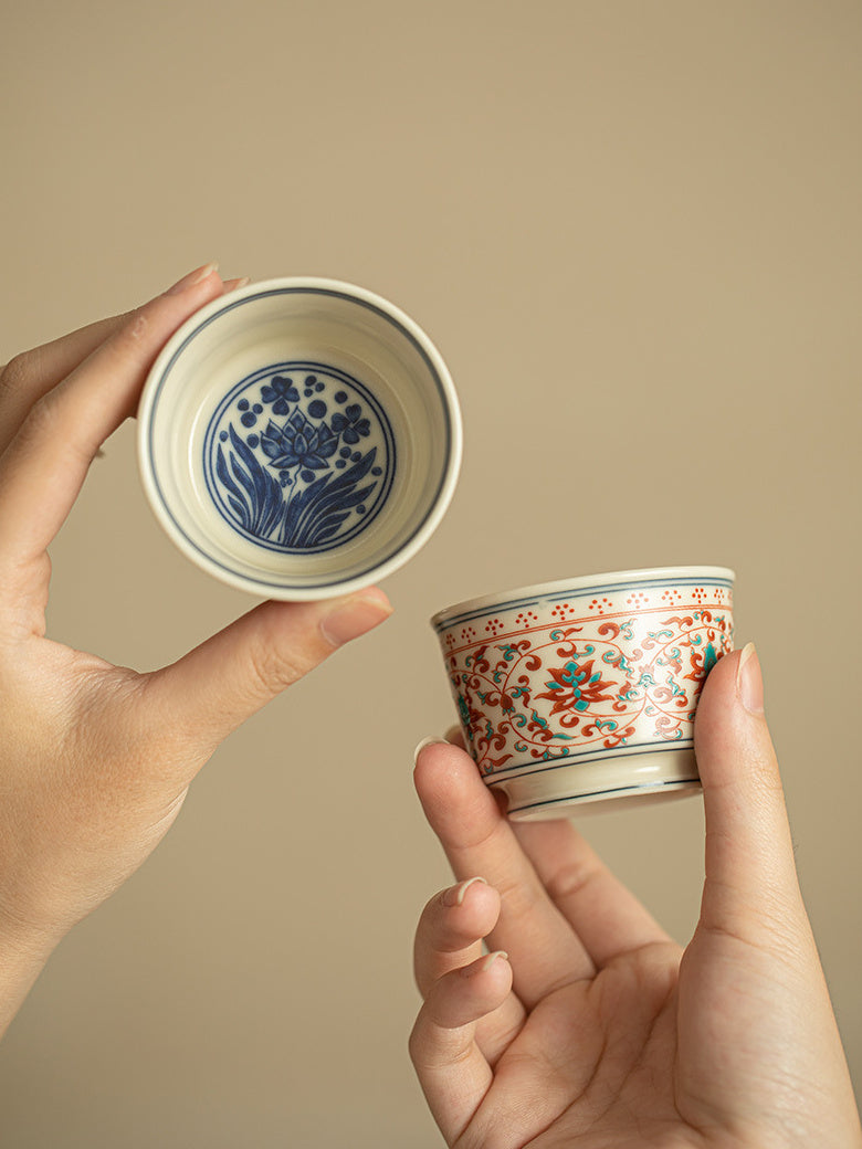 Two matching ceramic tea cups showing the blue lotus interior and red-green exterior pattern