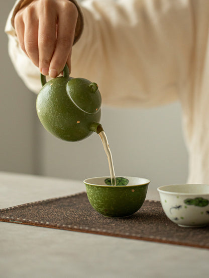 Hand pouring tea from the green mandarin-inspired ceramic teapot into a green fish-motif teacup