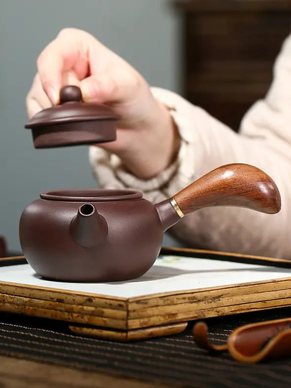 Hand lifting the lid from a handmade Yixing zisha side-handle teapot