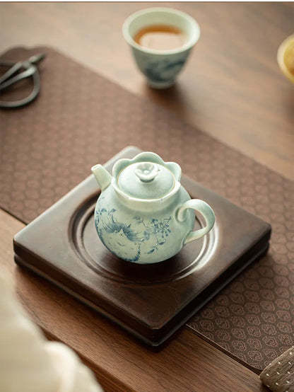 Top-angle view of the cat ceramic teapot on a square wooden tea stand with a cup nearby
