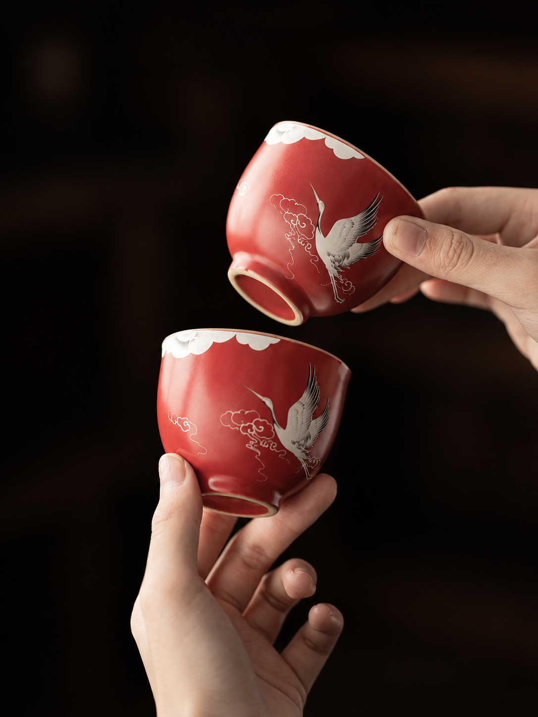 Close-up of two red ceramic teacups with crane and cloud motifs
