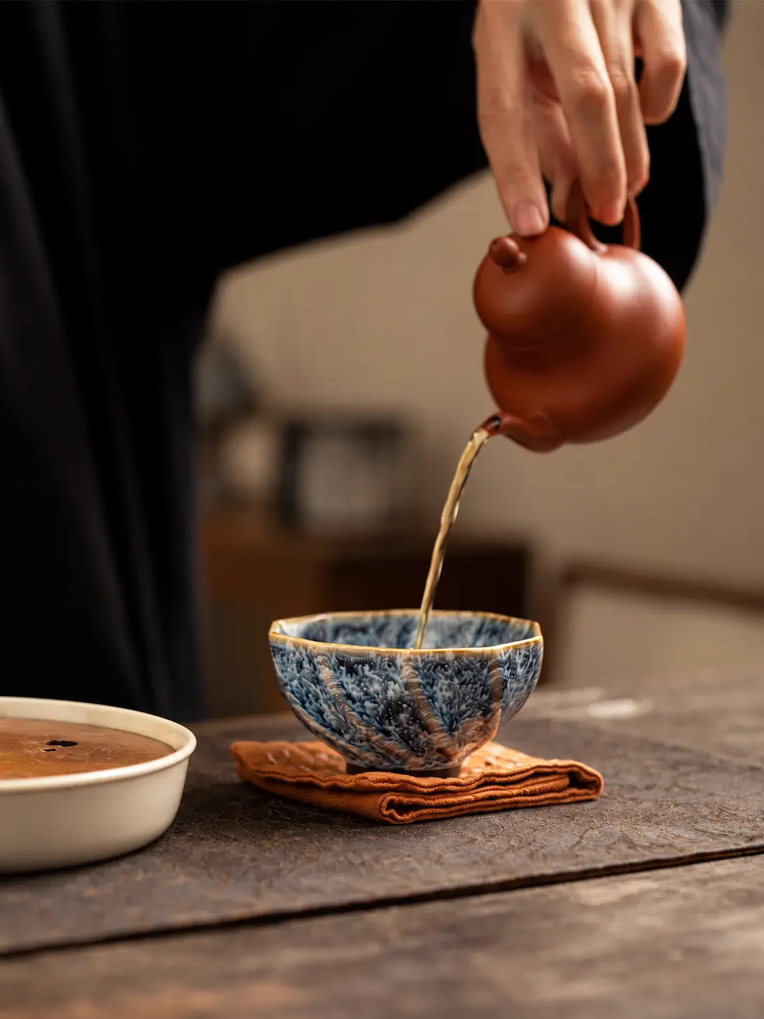Tea being poured from a clay teapot into a blue-and-white faceted gongfu tea cup