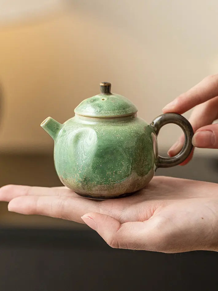 Close view of the green reactive-glaze teapot and side handle held in two hands
