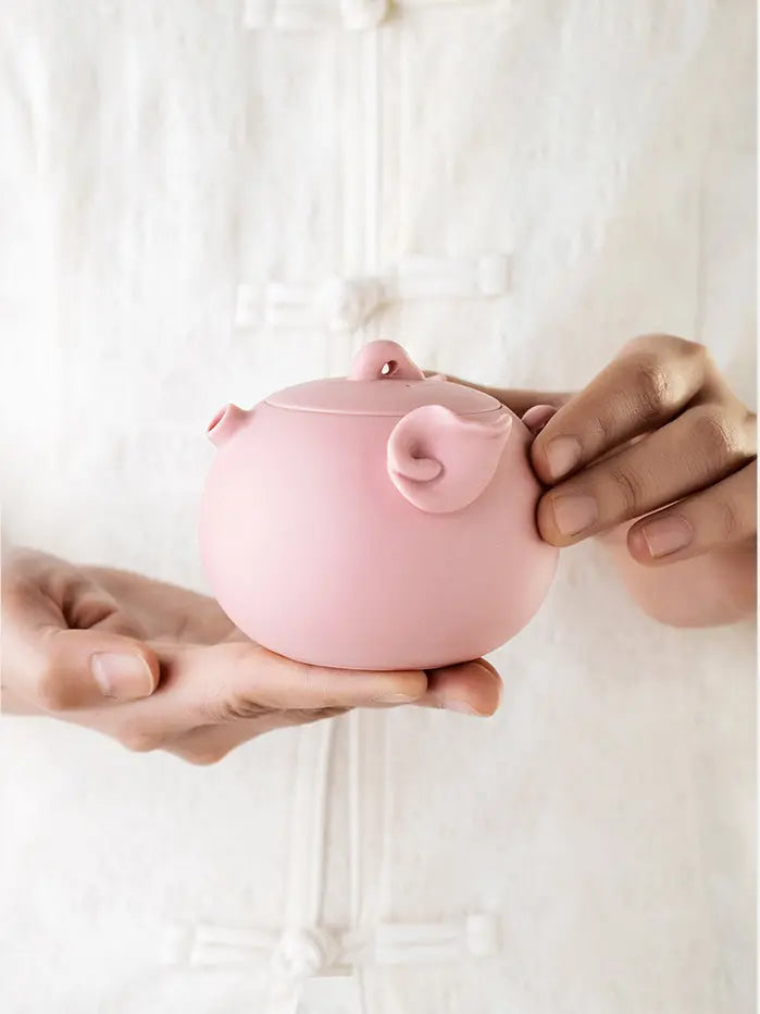 Pink pig-shaped zisha teapot displayed in both hands
