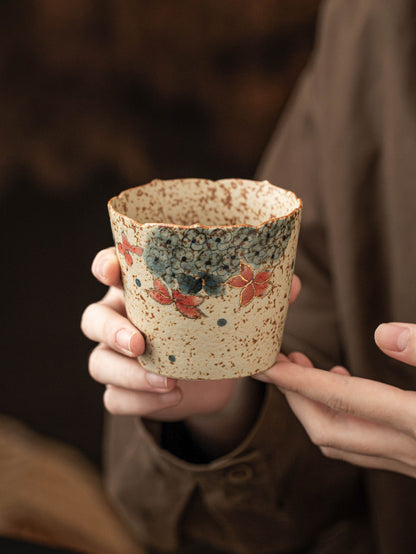 Two hands holding the wide-rim hydrangea ceramic coffee cup to show its size and painted design