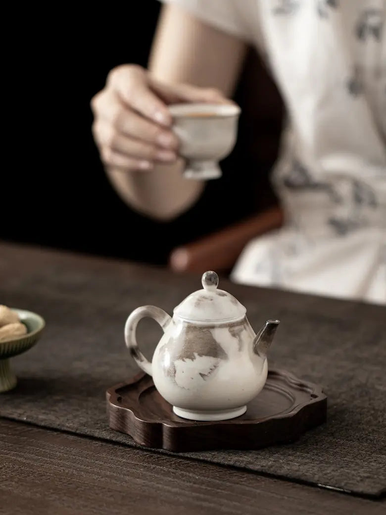 Ink-wash ceramic teapot on a wooden tea tray with a person holding a teacup