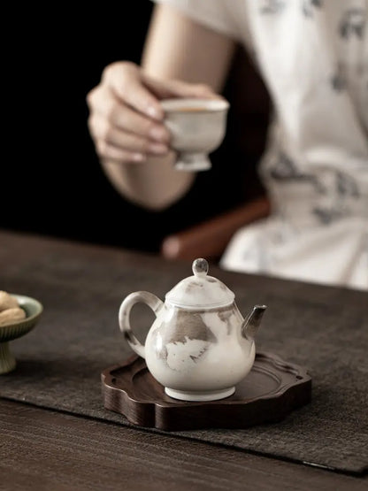Ink-wash ceramic teapot on a wooden tea tray with a person holding a teacup