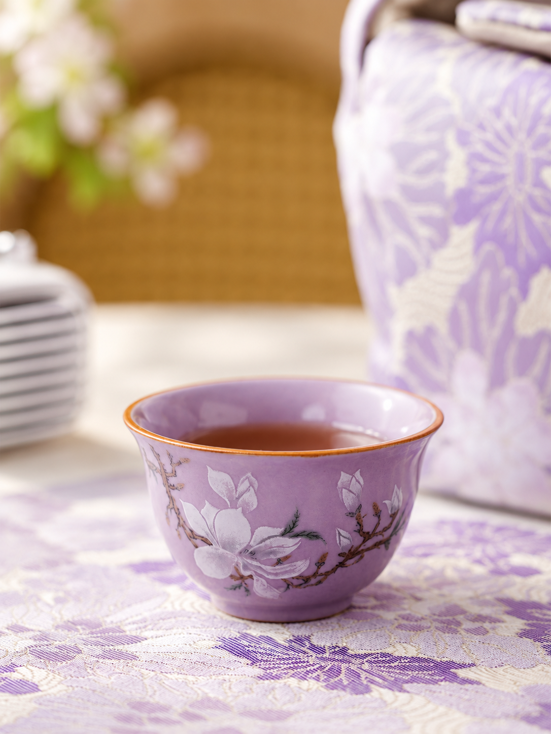 Close-up of a purple teacup with a white magnolia motif and warm-toned rim
