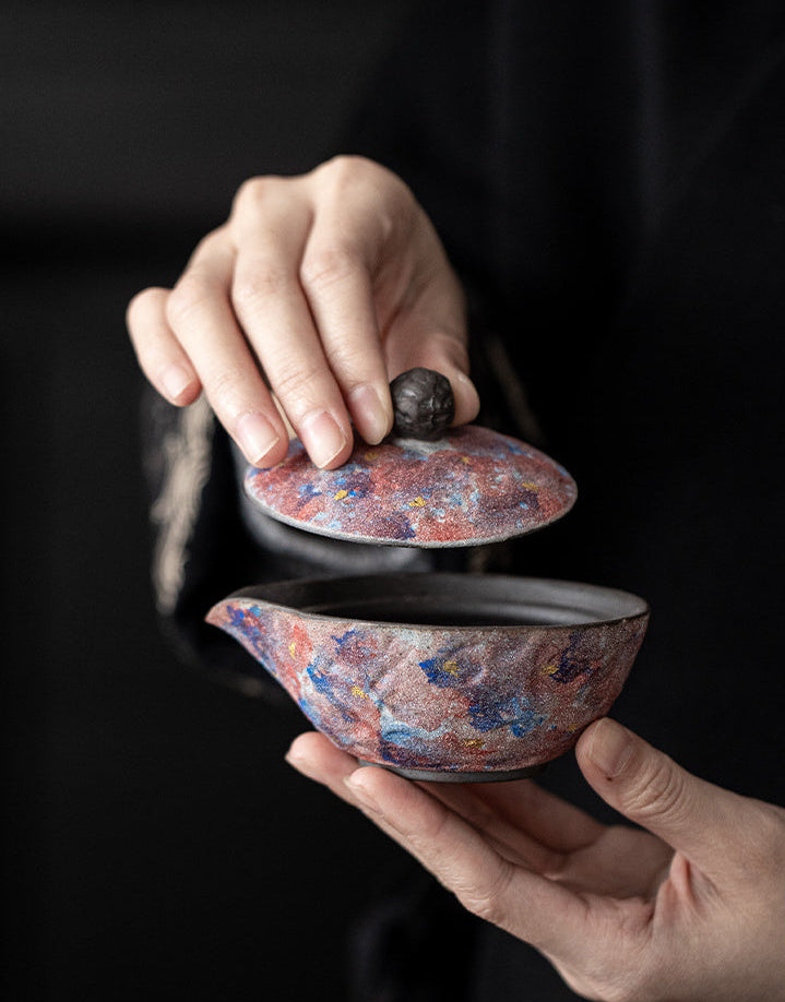 Hands lifting the lid from a galaxy glaze handleless ceramic teapot

