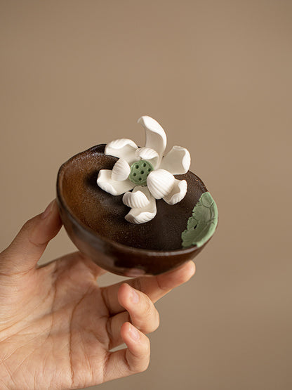 Hand holding a brown ceramic tea cup with sculpted white lotus flowers