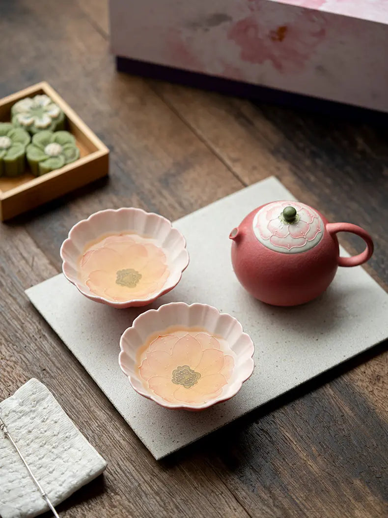 Pink lotus ceramic tea set for two with brewed tea in both flower-shaped cups
