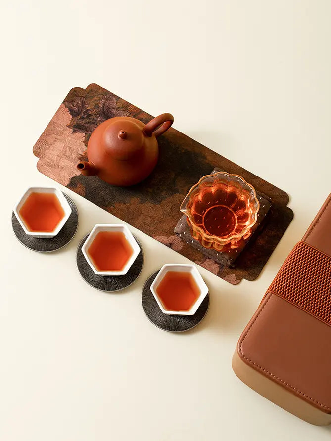 Overhead view of a portable gongfu tea set with three ceramic cups and glass pitcher
