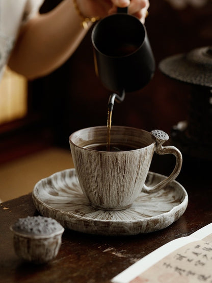 Dark coffee being poured into a handmade lotus pod ceramic cup resting on the matching round plate