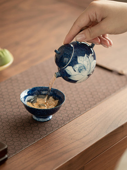 Blue lotus ceramic teapot pouring tea into a tea bowl

