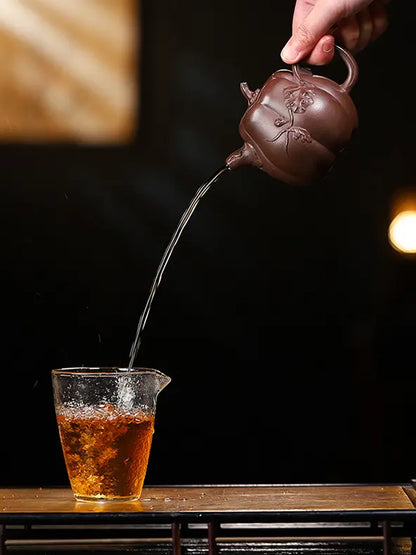 Hand pouring amber tea from a pumpkin-shaped zisha teapot into a clear glass pitcher