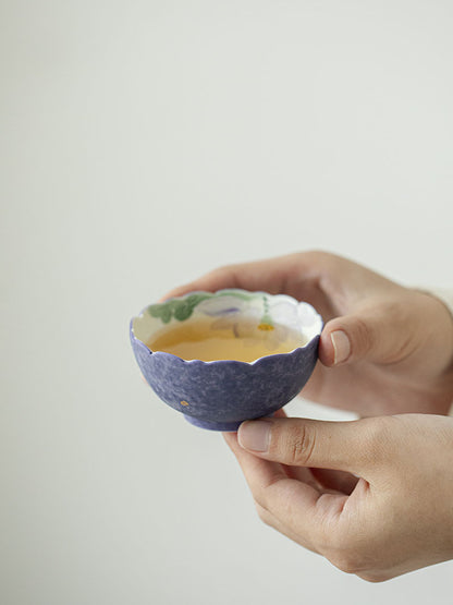 Purple flower-rim ceramic teacup filled with tea, showing the hand-painted lotus interior