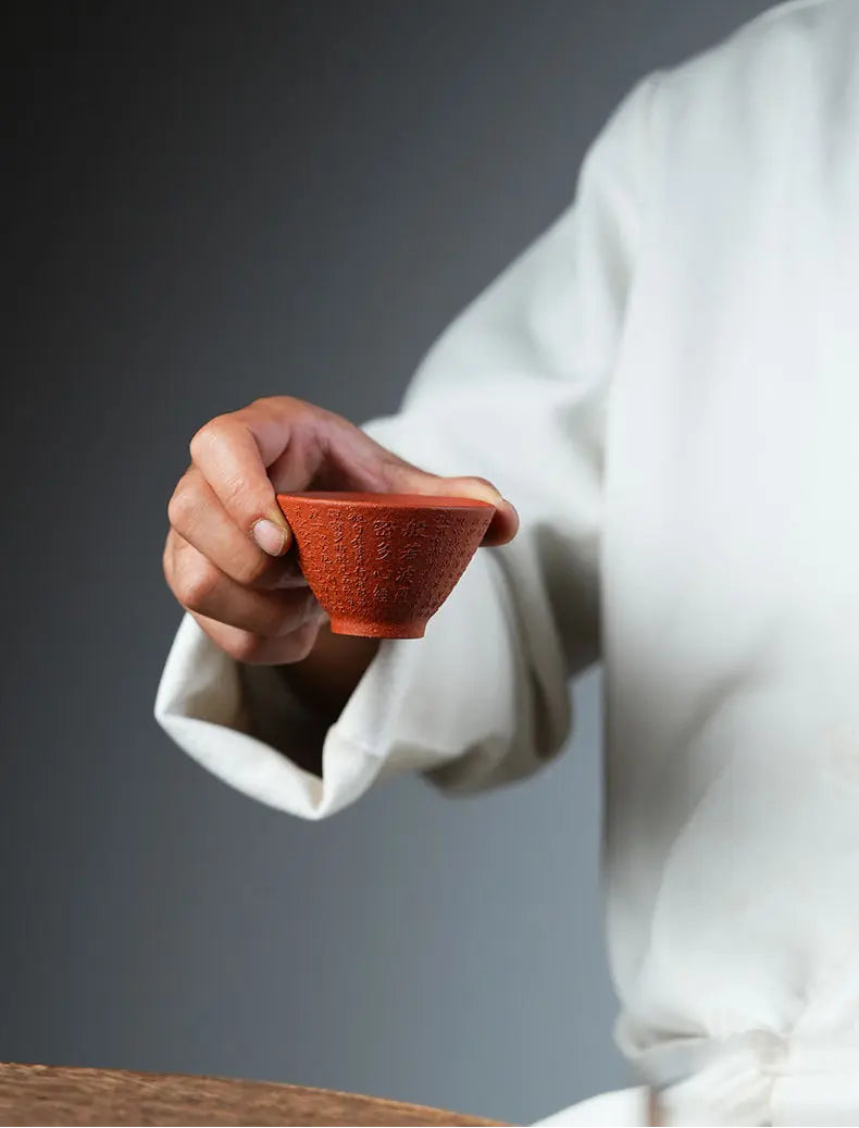 Person holding a reddish-brown Heart Sutra zisha tea cup