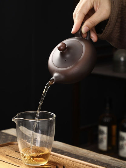 Handmade Yixing Zisha teapot pouring tea into a glass pitcher