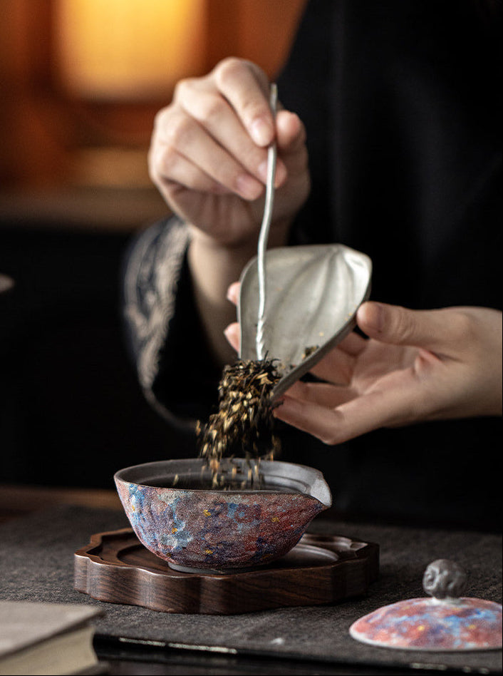 Loose tea leaves being added to an open galaxy glaze ceramic teapot
