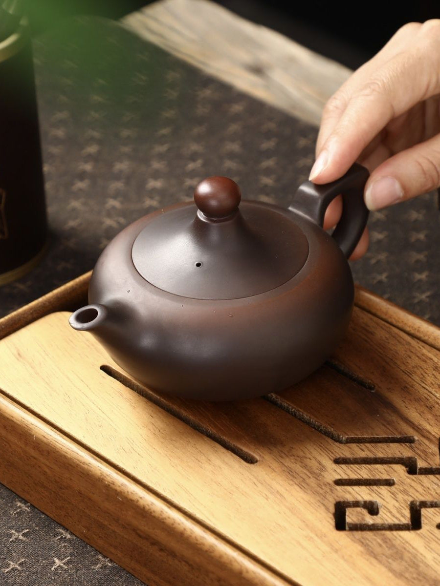 Deep brown matte Zisha teapot resting on a wooden tea tray