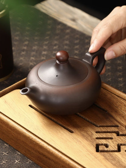 Deep brown matte Zisha teapot resting on a wooden tea tray