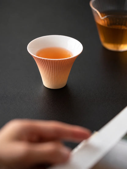 Gradient firework ceramic tasting cup filled with tea on a dark tabletop
