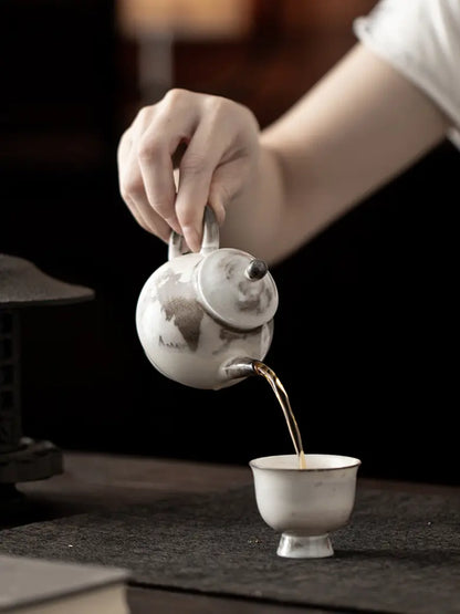 Hand pouring tea from the ink-wash ceramic teapot into a small teacup