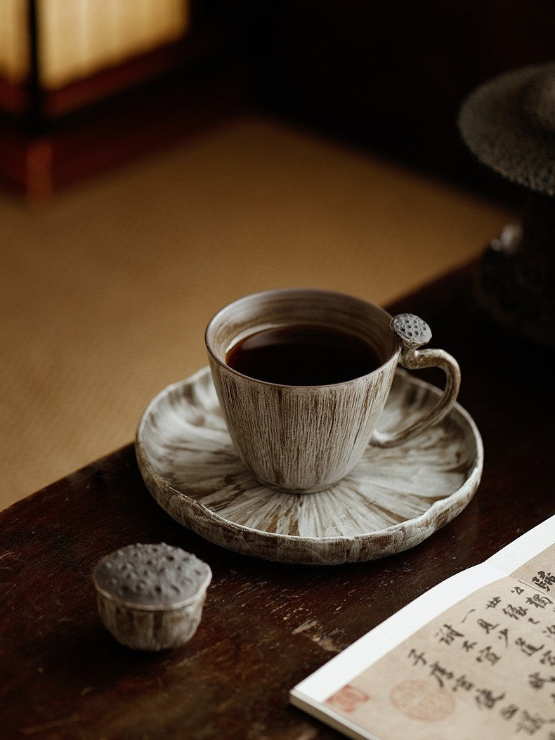 Gray-and-white lotus pod ceramic coffee cup with round plate, small ornament, and book
