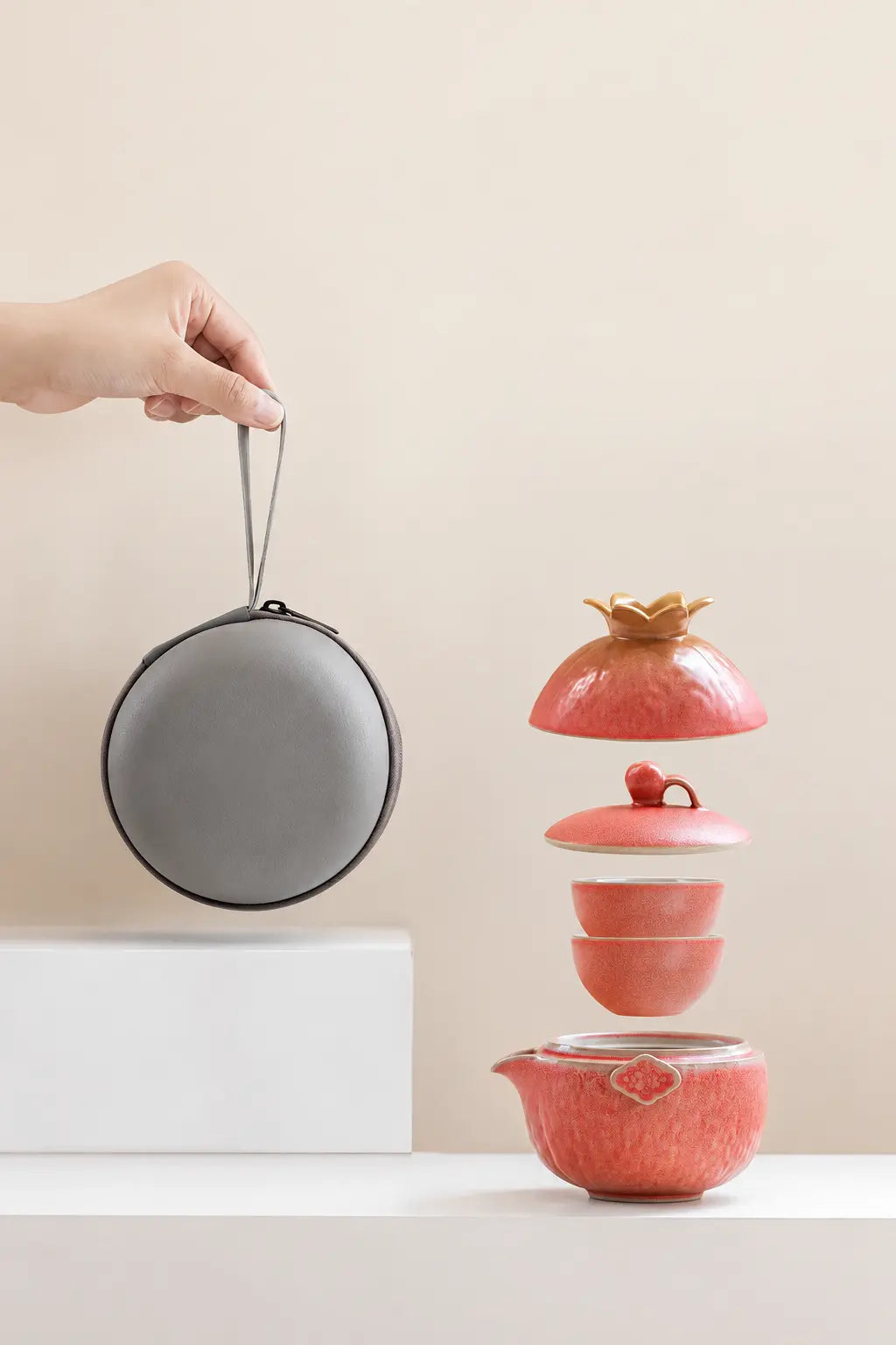 Nested components of the pomegranate travel tea set arranged beside the round carrying case
