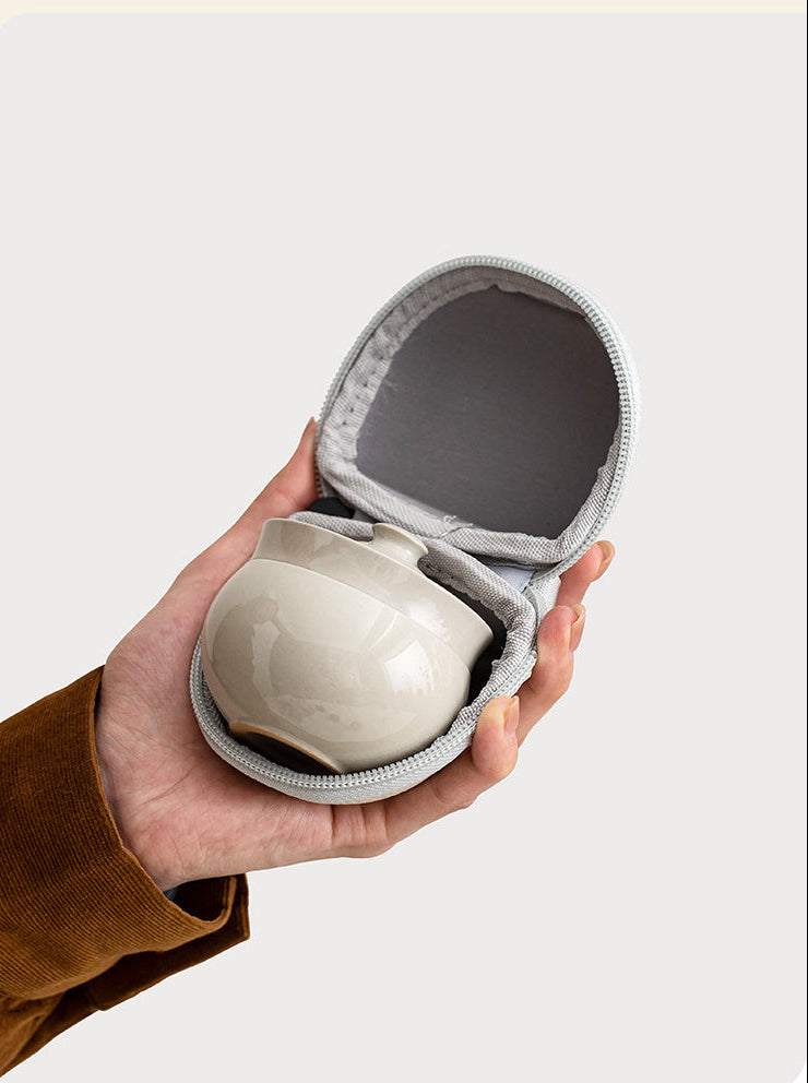 Open portable case held in one hand with the stacked gray ceramic tea set inside
