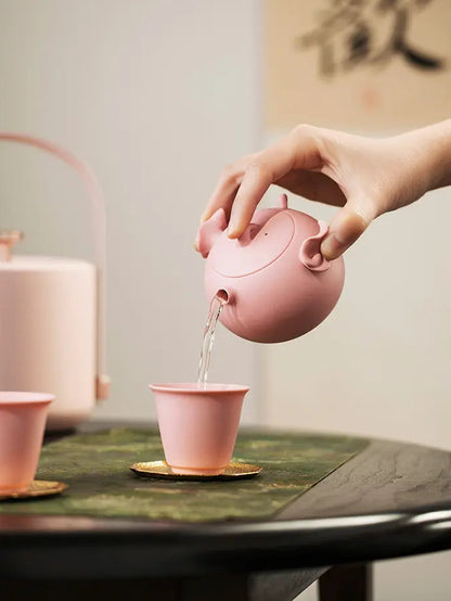 Pink zisha pig teapot pouring tea into a matching cup
