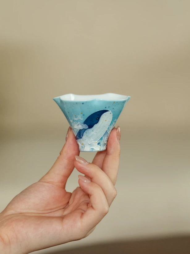 Small blue whale flower-rim gongfu tea cup held between two fingers