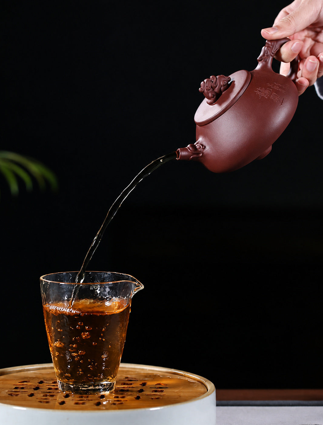Hand pouring tea from the Yixing dragon teapot into a clear glass cup