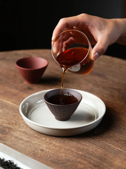 Tea poured from a glass pitcher into a dark brown Heart Sutra zisha tea cup