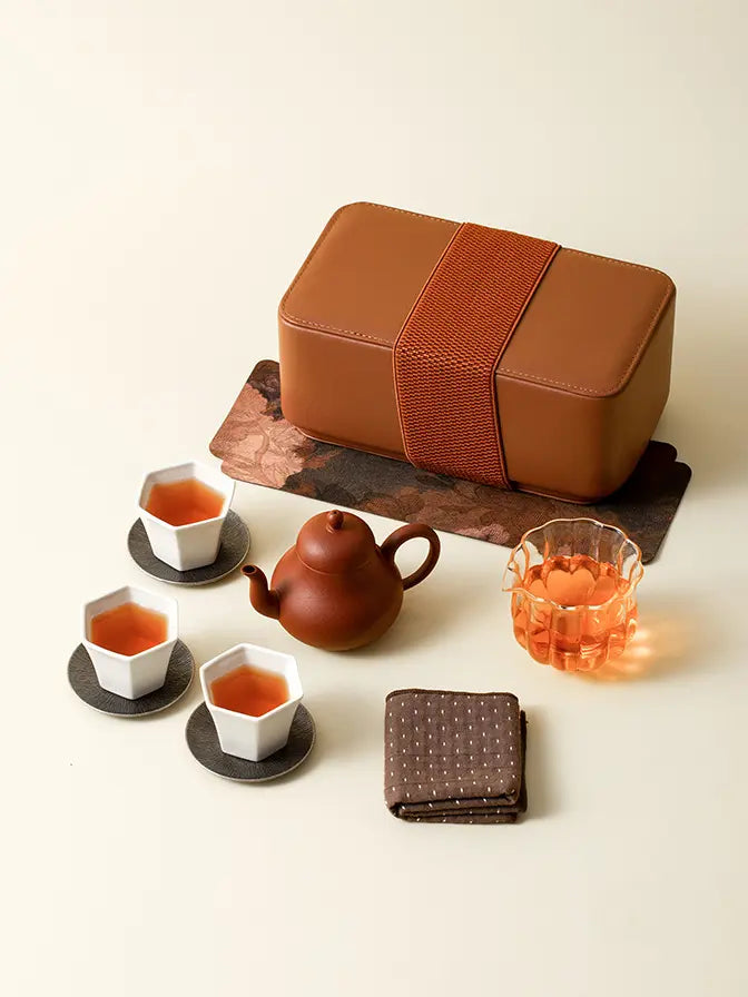Portable tea set displayed with its brown storage case on a warm ivory table

