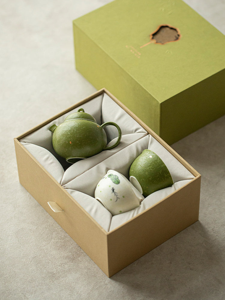 Green ceramic teapot and two hand-painted teacups arranged inside the fitted gift box