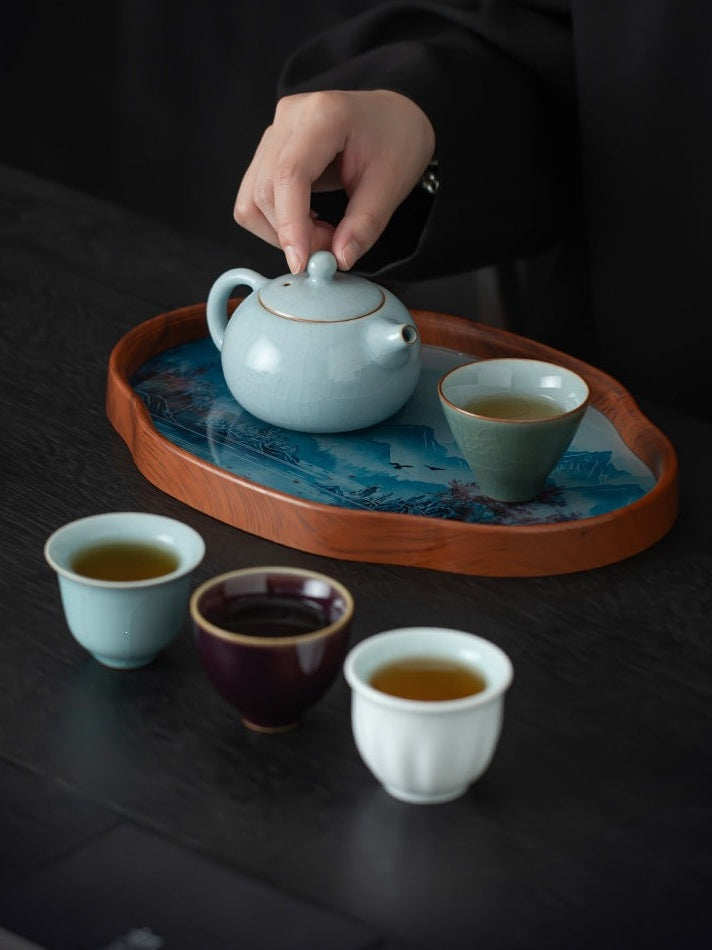 Pale blue Xishi teapot and four tasting cups arranged on a landscape tea tray for tea service
