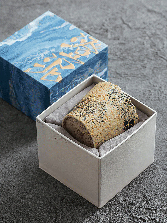 Sunflower-pattern ceramic coffee cup arranged inside an open blue gift box
