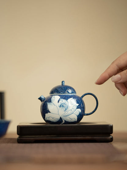 Compact blue and white lotus teapot displayed on a dark wooden stand
