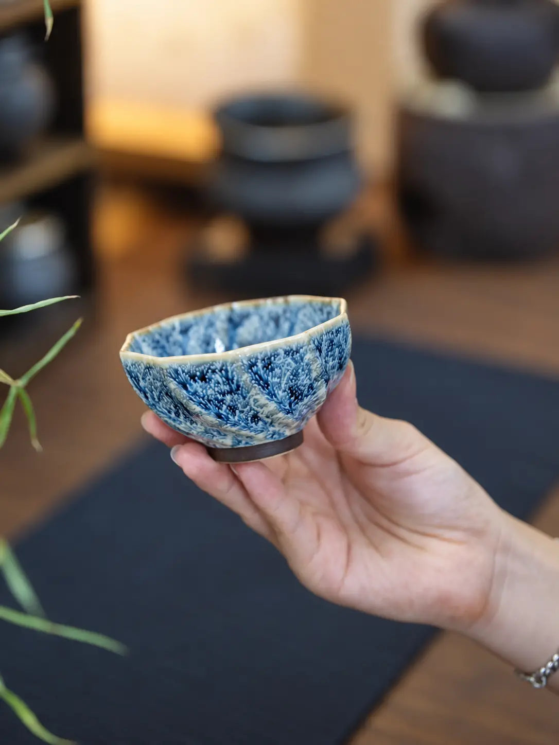 Hand holding a low-profile faceted ceramic tea cup to show its size and glaze