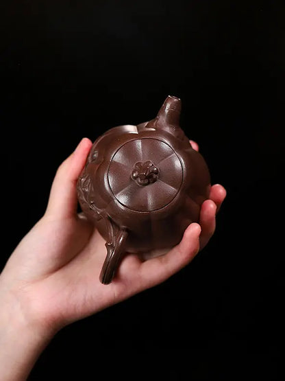 Hand holding a pumpkin zisha teapot to show its lid, stem-shaped knob, and compact scale